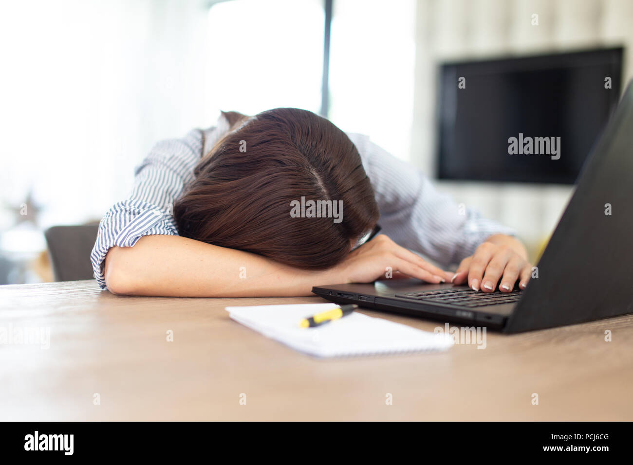 Stanco brunette donna che dorme nella parte anteriore del computer portatile per interni Foto Stock