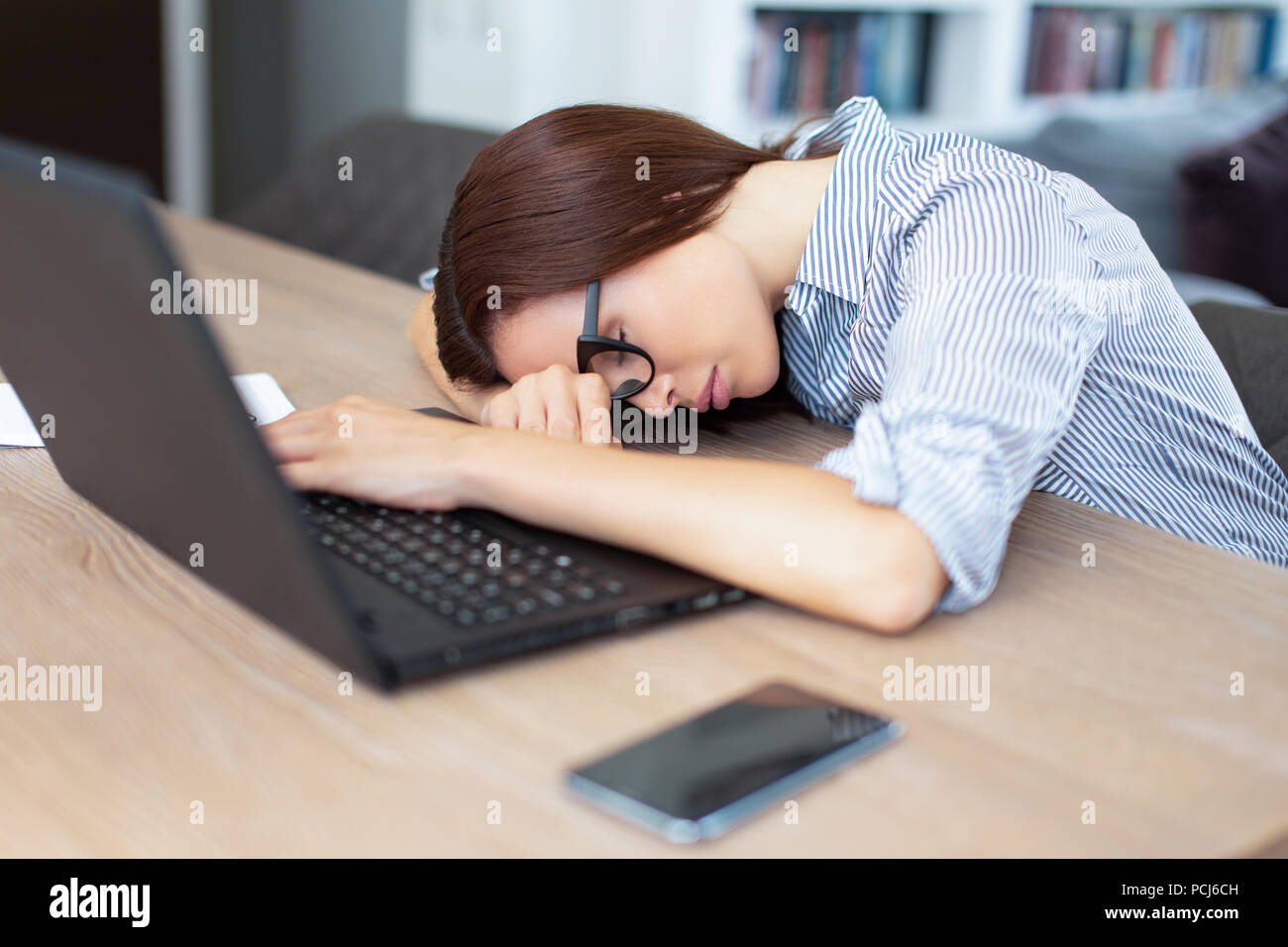 Stanco bruna giovane donna che dorme nella parte anteriore del computer portatile per interni Foto Stock