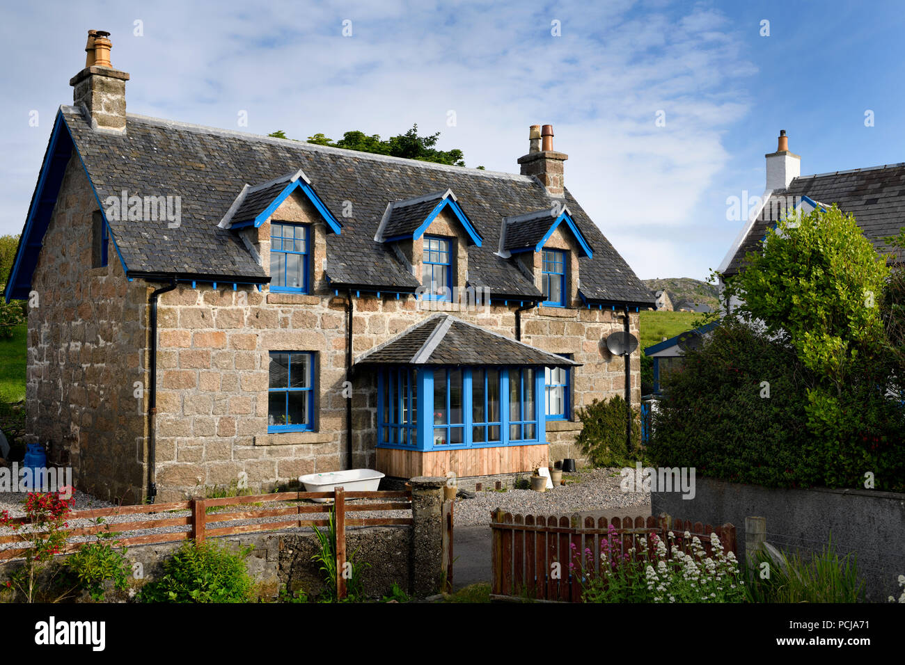 Casa in pietra con rivestimento blu e giardino fiorito sulla strada principale di Baile Mor villaggio sull isola di Iona Ebridi Interne in Scozia UK Foto Stock