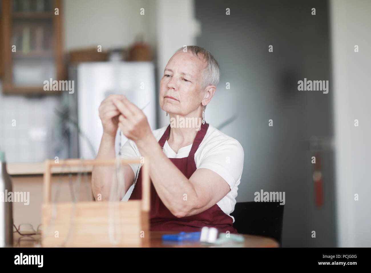 Donna seduta al tavolo che fissa una collana Foto Stock