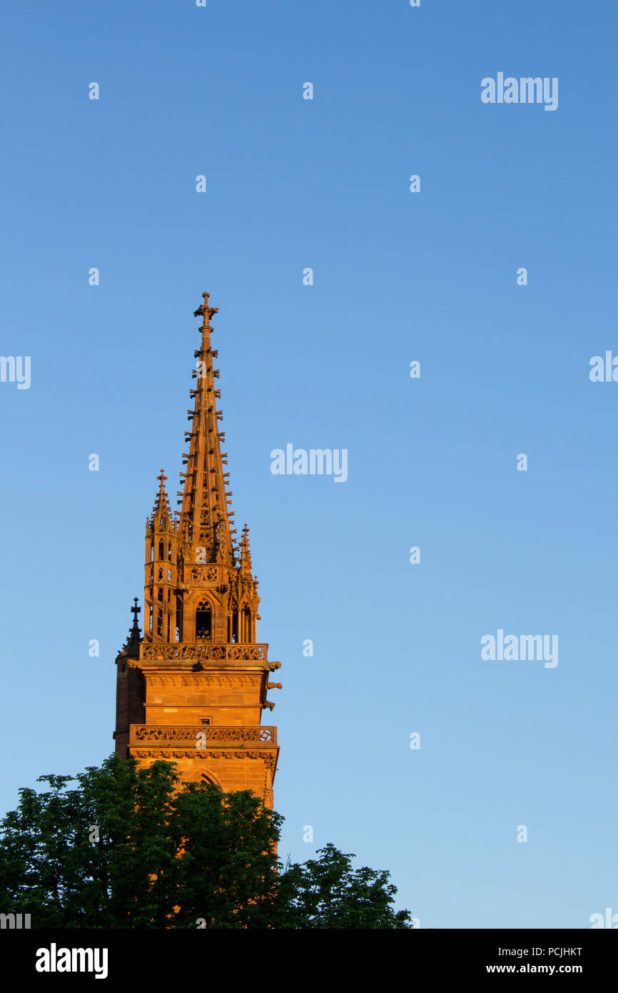 La torre della cattedrale di Basilea (chiesa e ex cattedrale) a Basilea, in Svizzera. Incandescente di rosso e di giallo al tramonto. Foto Stock