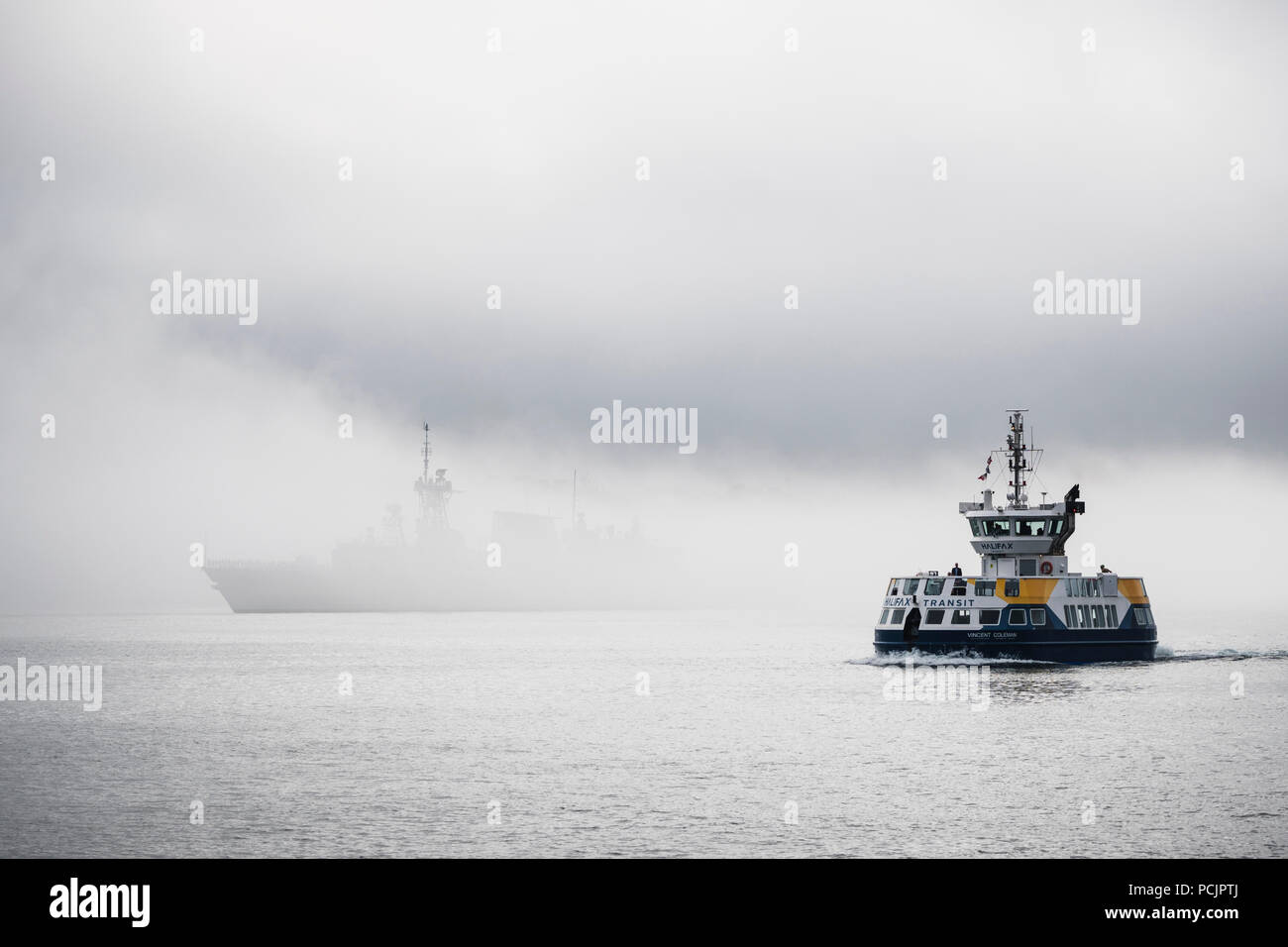 Porto traghetto passa come Halifax-classe fregata HMCS ST. JOHN'S torna a Halifax, Nova Scotia, Canada, nella nebbia da un dispiegamento della NATO all'estero. Foto Stock
