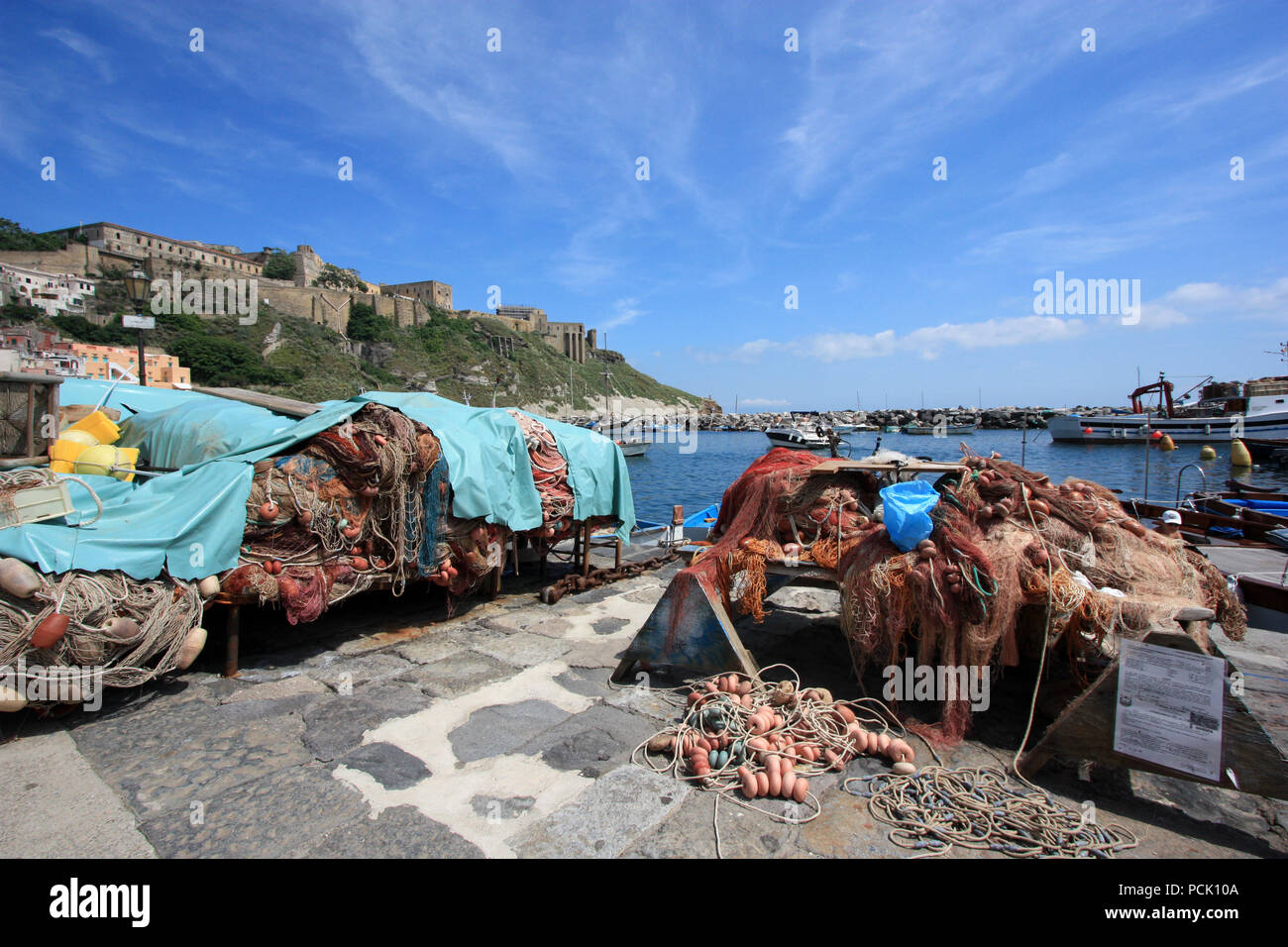 Rack di reti da pesca presso il lungomare della Corricella a Procida, Golfo di Napoli, Italia, con l'ex carcere di Terra Murata in background Foto Stock