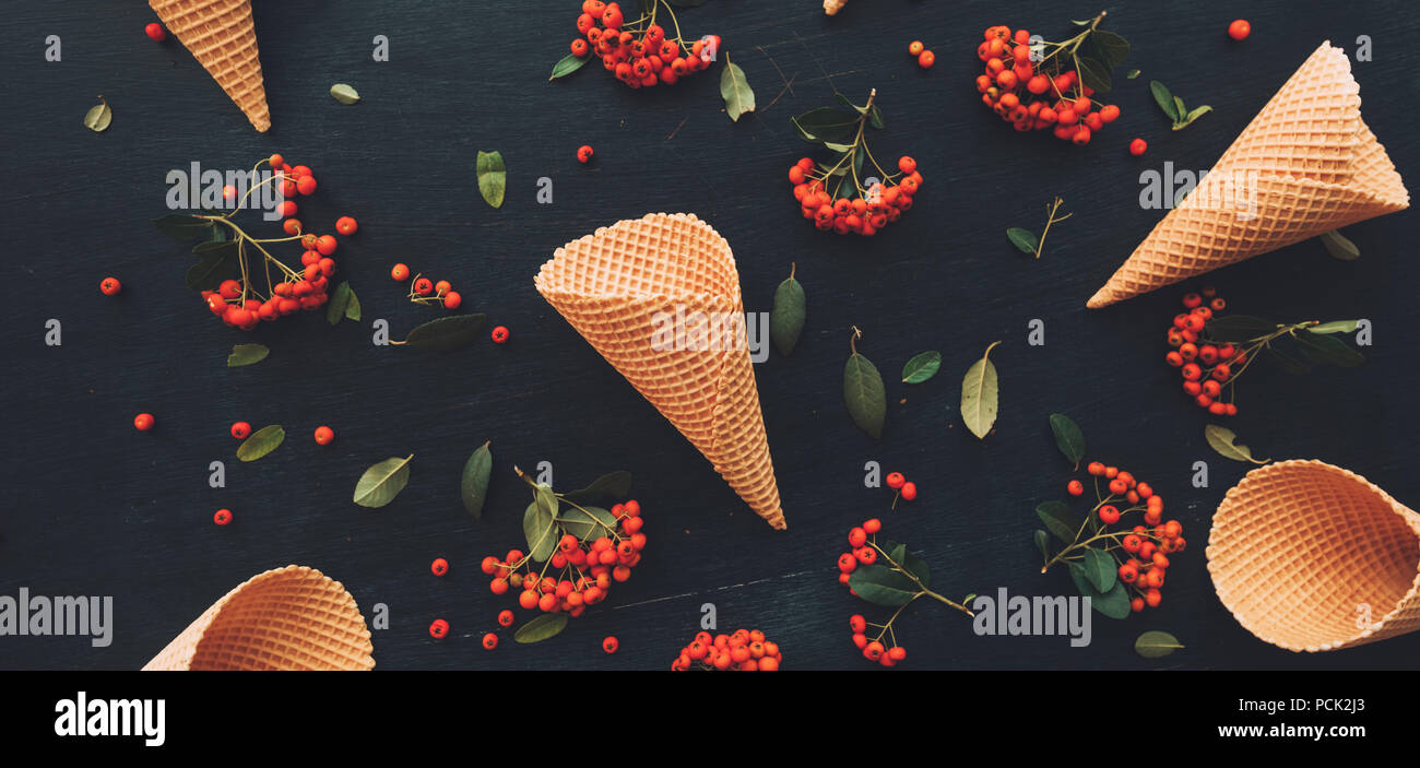 Waffle cono gelato flat top laici vista sul nero scuro dello sfondo in legno decorata con frutti di bosco la disposizione di frutta Foto Stock