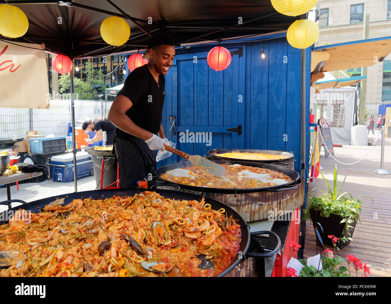 Un giovane uomo di preparare un enorme piatto di paella in un outdoor street food kiosk presso Bouffons Montreal Foto Stock