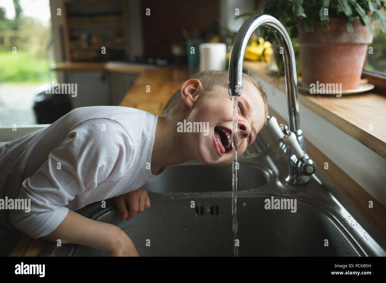 Ragazzo di bere acqua dal rubinetto in cucina Foto Stock