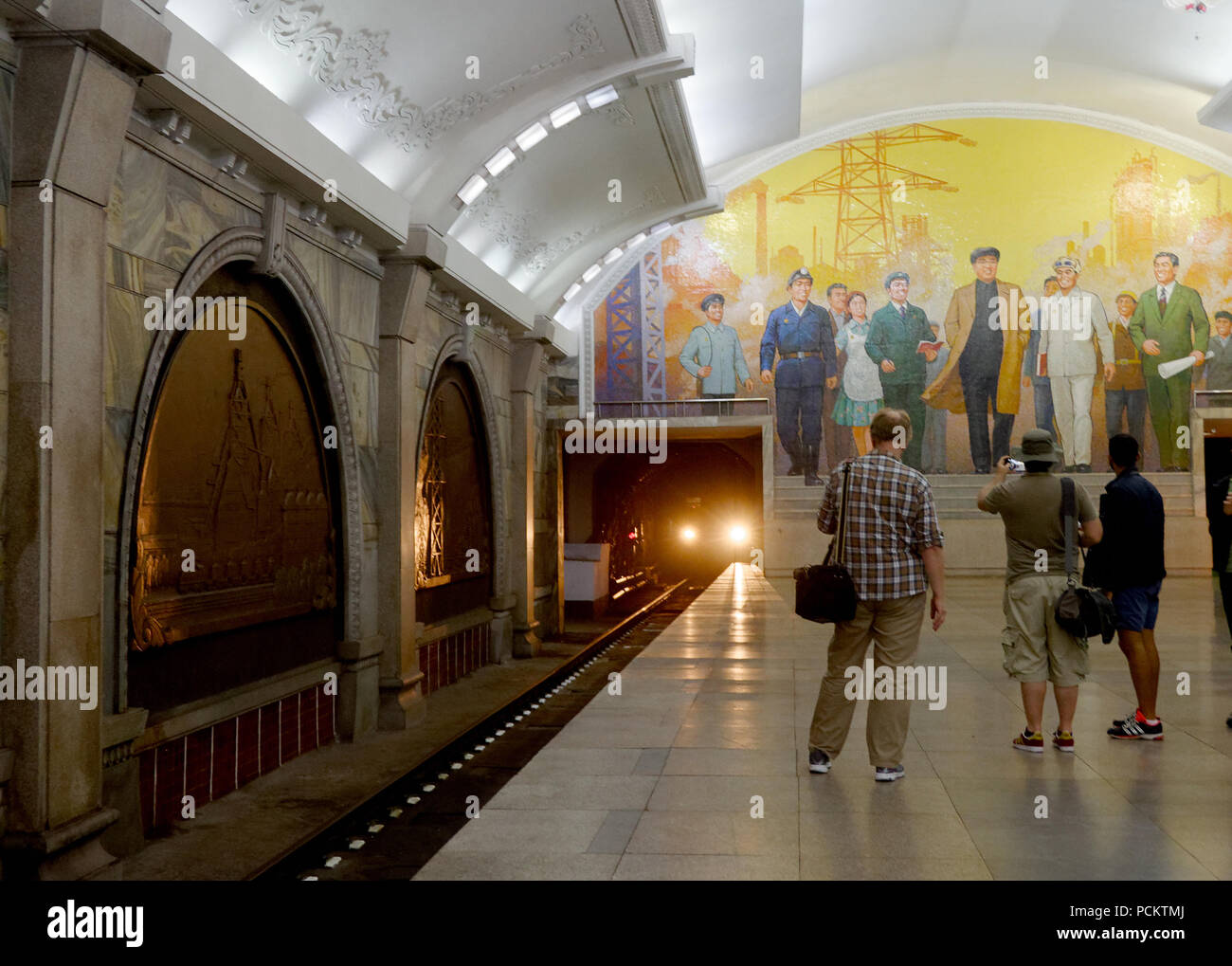 I turisti a guardare a fotografare un treno della metropolitana come si arriva nella stazione di Revival piattaforma, Metropolitana di Pyongyang, Corea del Nord Foto Stock