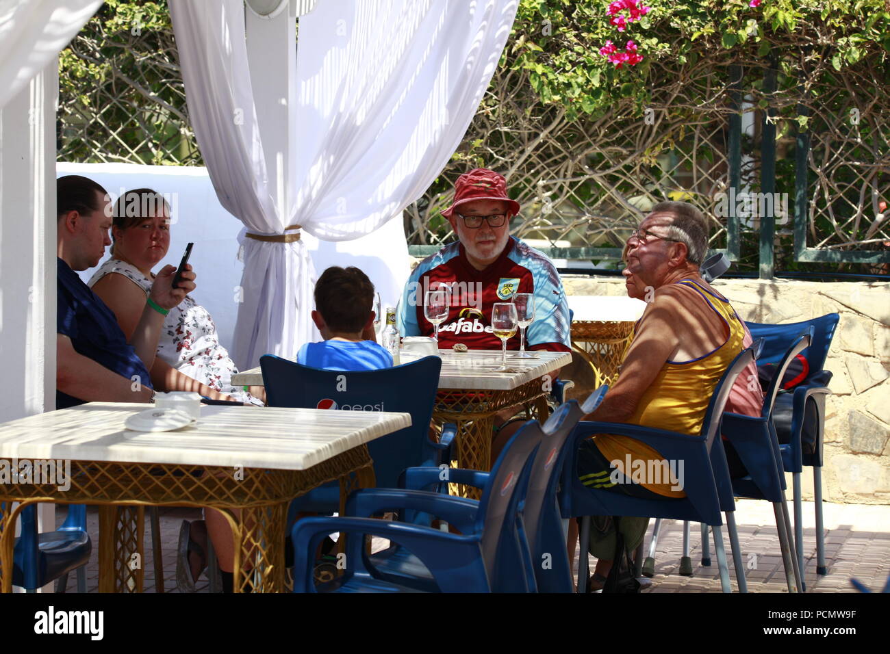 Roquetas de Mar Almeria, Spagna. Il 3° agosto 2018. L'ondata di caldo che sta colpendo la Spagna dovrebbe superare i 45°C in alcune parti del paese. Una famiglia di turisti britannici all'estero sedersi e bere fuori in un ristorante all'aperto, un uomo si siede indossando una maglietta di calcio. Photo credit: Paolo Lawrenson /Alamy Live News Foto Stock