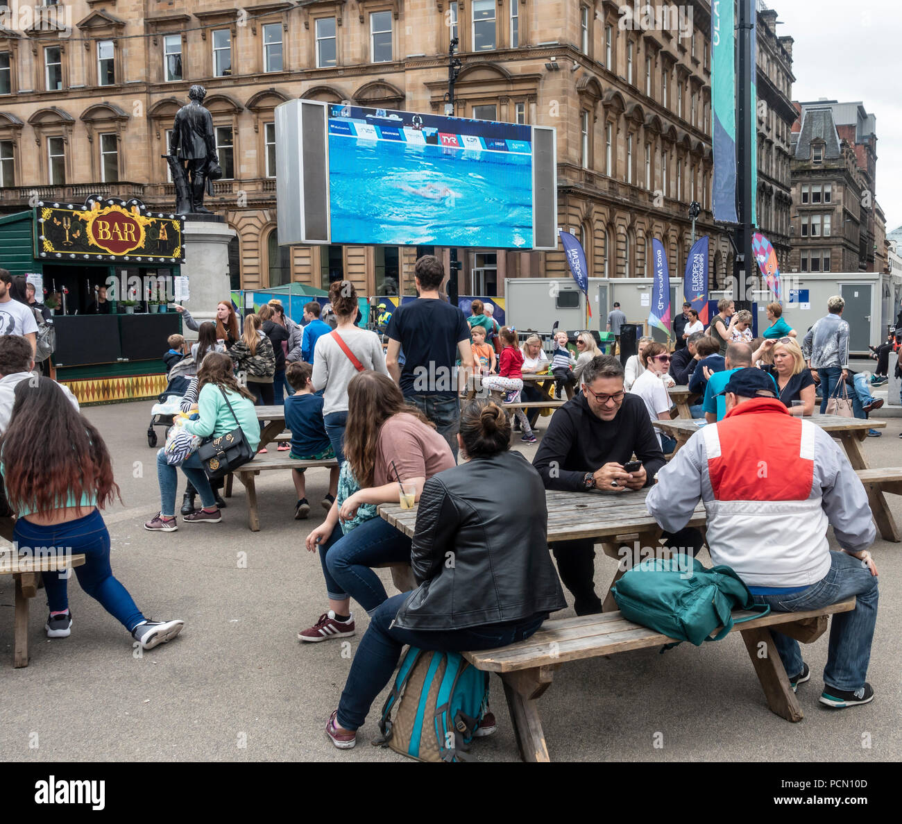 George Square; Glasgow, in Scozia. 03 agosto 2018. La gente fuori e circa in George Square nel centro di Glasgow e rilassante godendo Festival 2018. Il festival è in esecuzione in parallelo con i Campionati Europei di Glasgow 2018. George Square è un luogo libero con diversi live e attrazioni virtuale quotidianamente. Vi è un grande schermo che mostra la copertura dal vivo della competizione sportiva azione. In questa foto, nuoto sincronizzato viene mostrato. Credito: Elizabeth Leyden/Alamy Live News Foto Stock