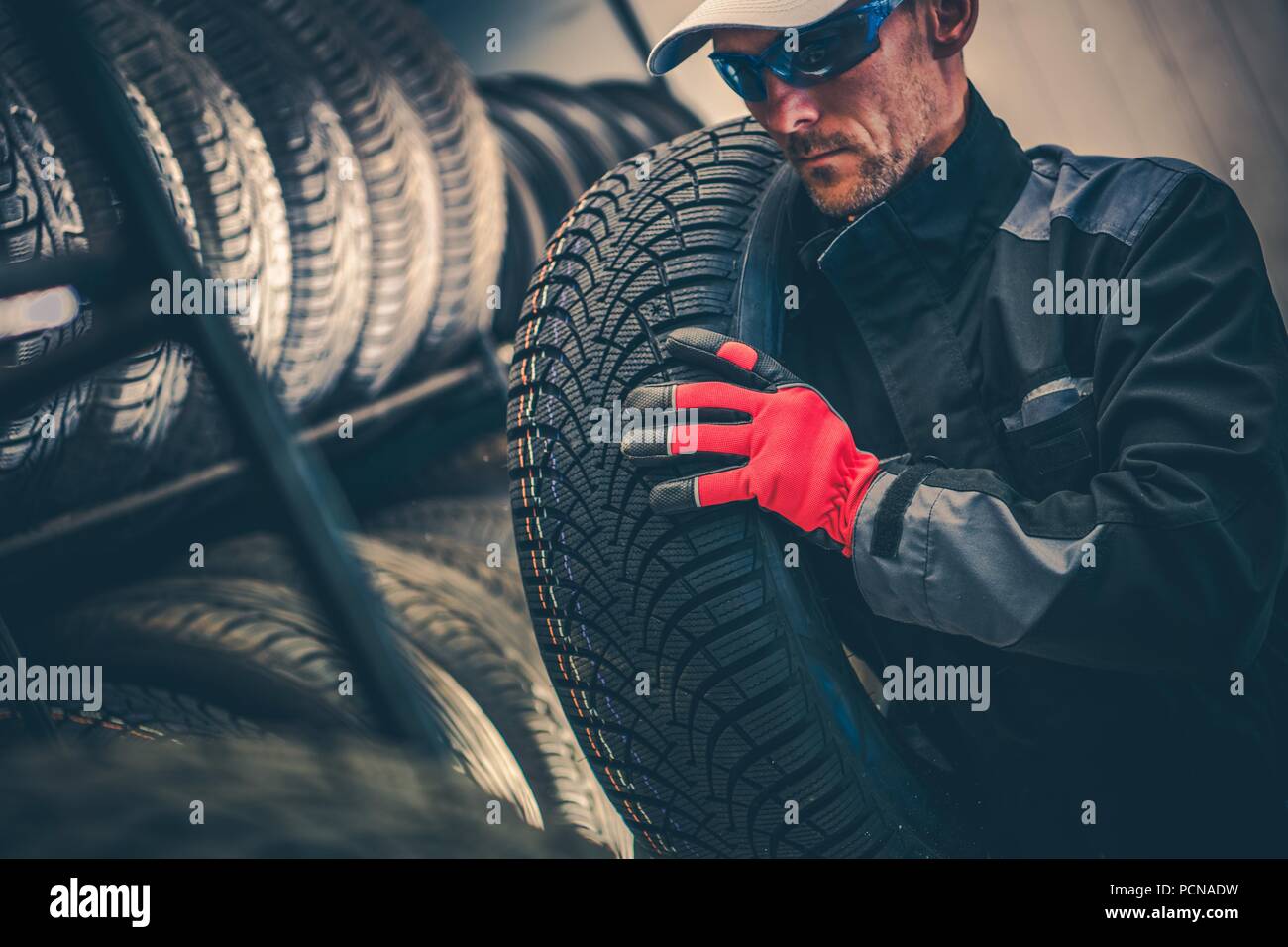 Servizio automatico di sostituzione del pneumatico del tema. Lavoratore caucasica nel suo 30s spostando la stagione invernale pneumatico. Foto Stock