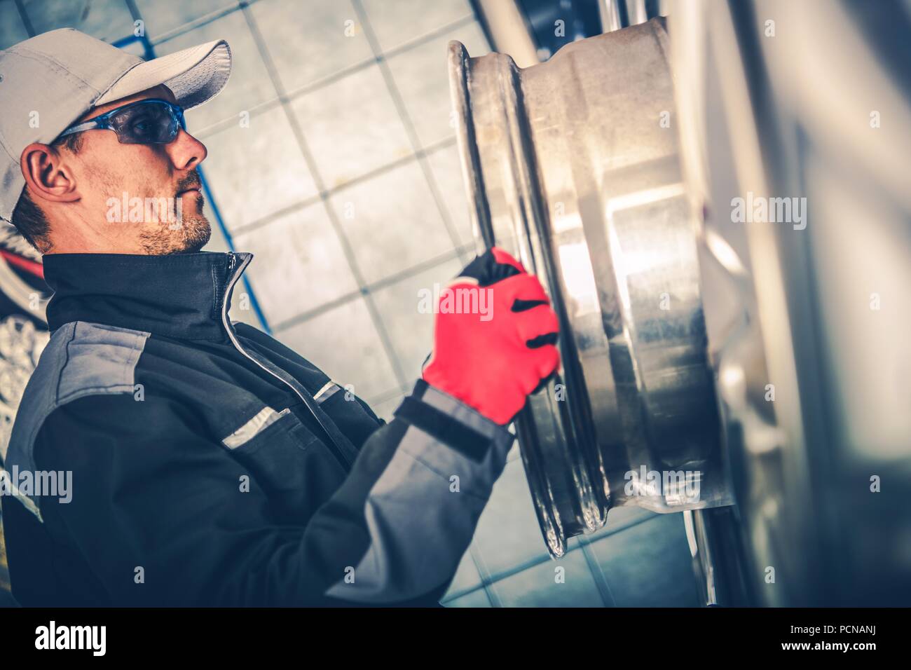 Lavoratore caucasica e la ruota in lega. Servizio pneumatici tecnico cercando la lega. Foto Stock