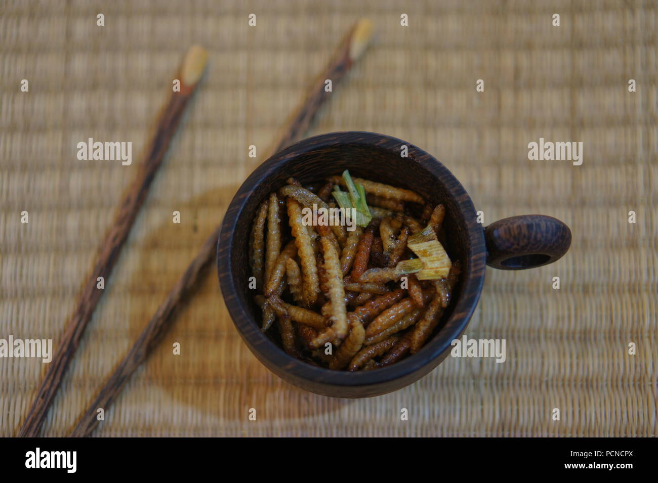 Gli insetti commestibili bruchi di bambù in coppa su un luogo di bambù mat Foto Stock