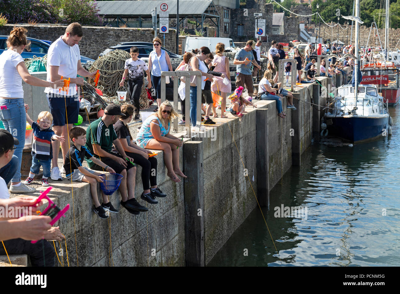 Turisti che si siedono sul bordo del molo a Conwy, il Galles del Nord, molti di loro la pesca dei granchi con una lenza. Foto Stock