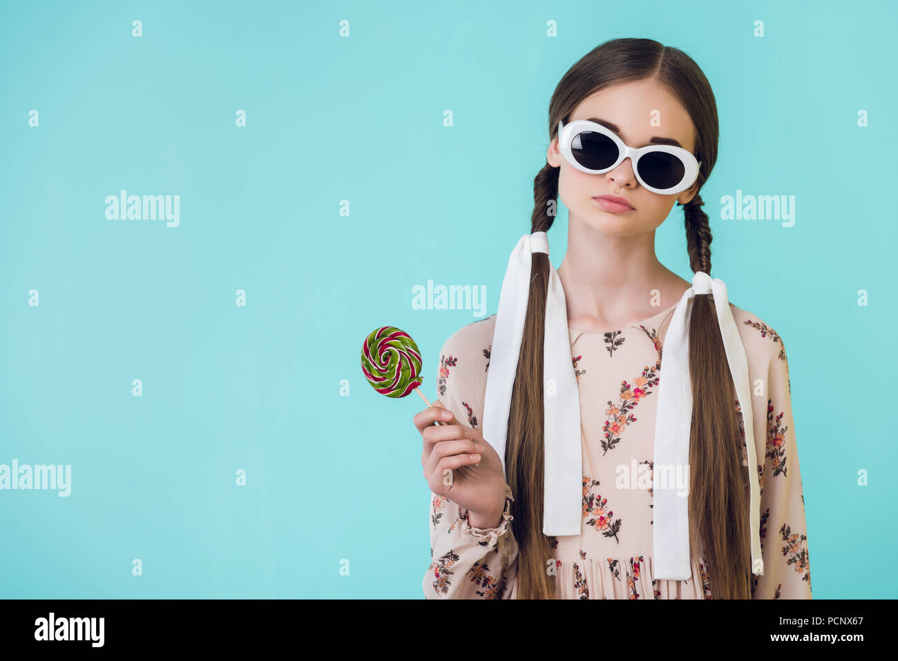 Moda ragazza teen in occhiali da sole con trecce holding lecca-lecca,  isolato su blu Foto stock - Alamy
