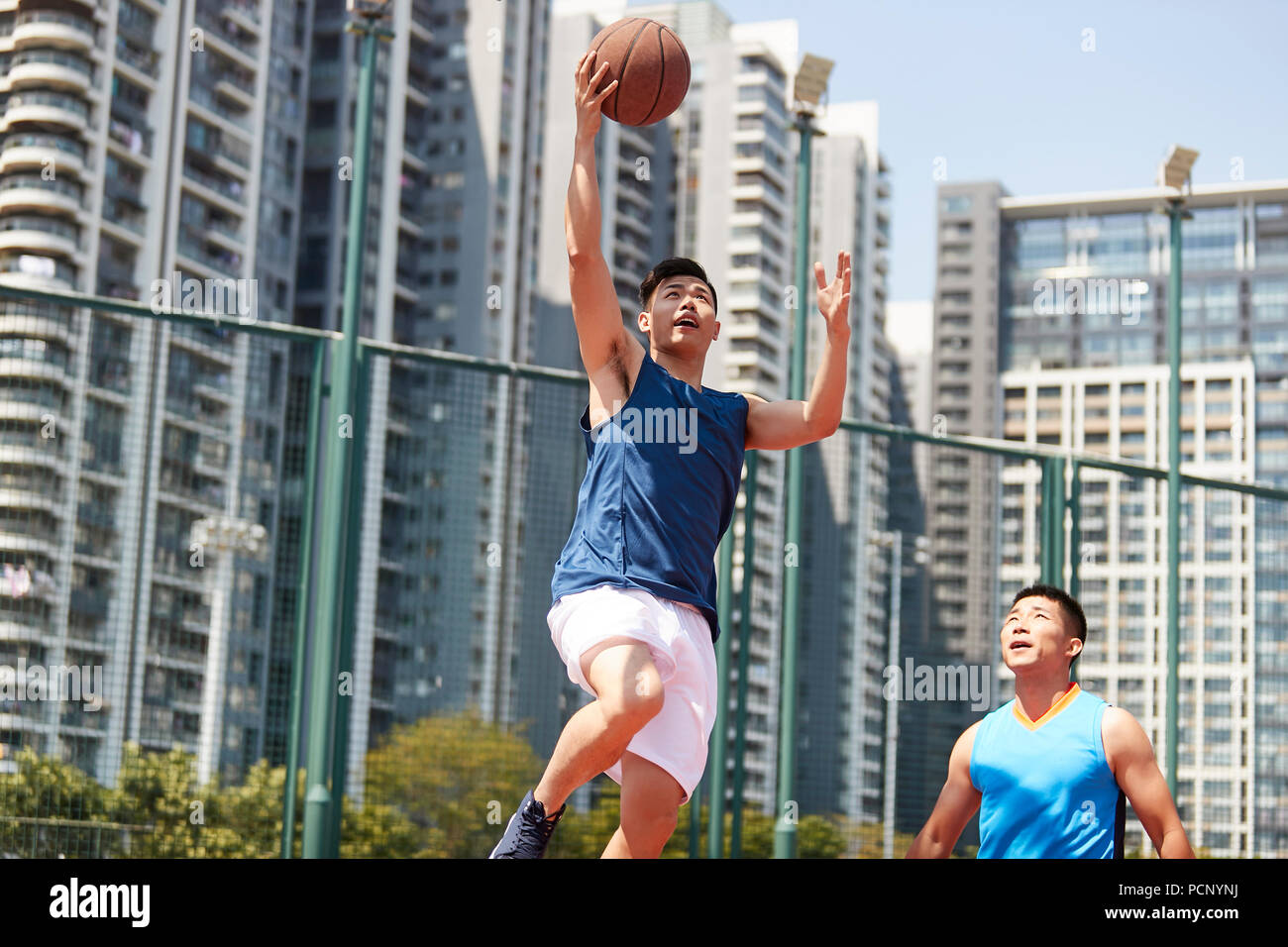 Giovani asiatici giocatore di basket salendo per un layup mentre avversario giocando la difesa. Foto Stock