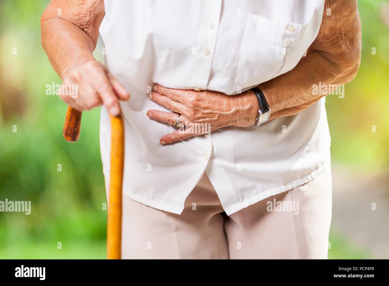 Donna anziana negli anni ottanta con un bastone da passeggio e dolori di stomaco Foto Stock