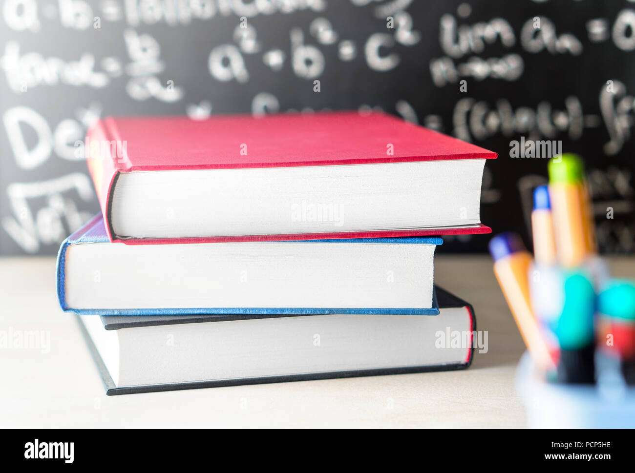 Pila e pila di libri sul tavolo di fronte a una lavagna in aula scolastica. Istruzione, lo studio, l'insegnamento o del concetto di conoscenza. Foto Stock