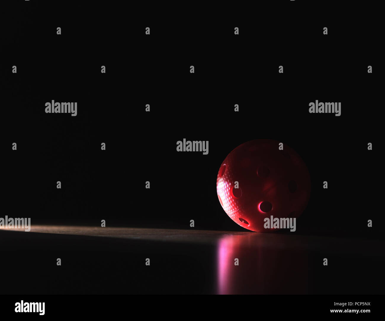 Nero e scuro dello sfondo sul floorball con copia negativo dello spazio. Sfera rossa in Spotlight in ombra. Foto Stock