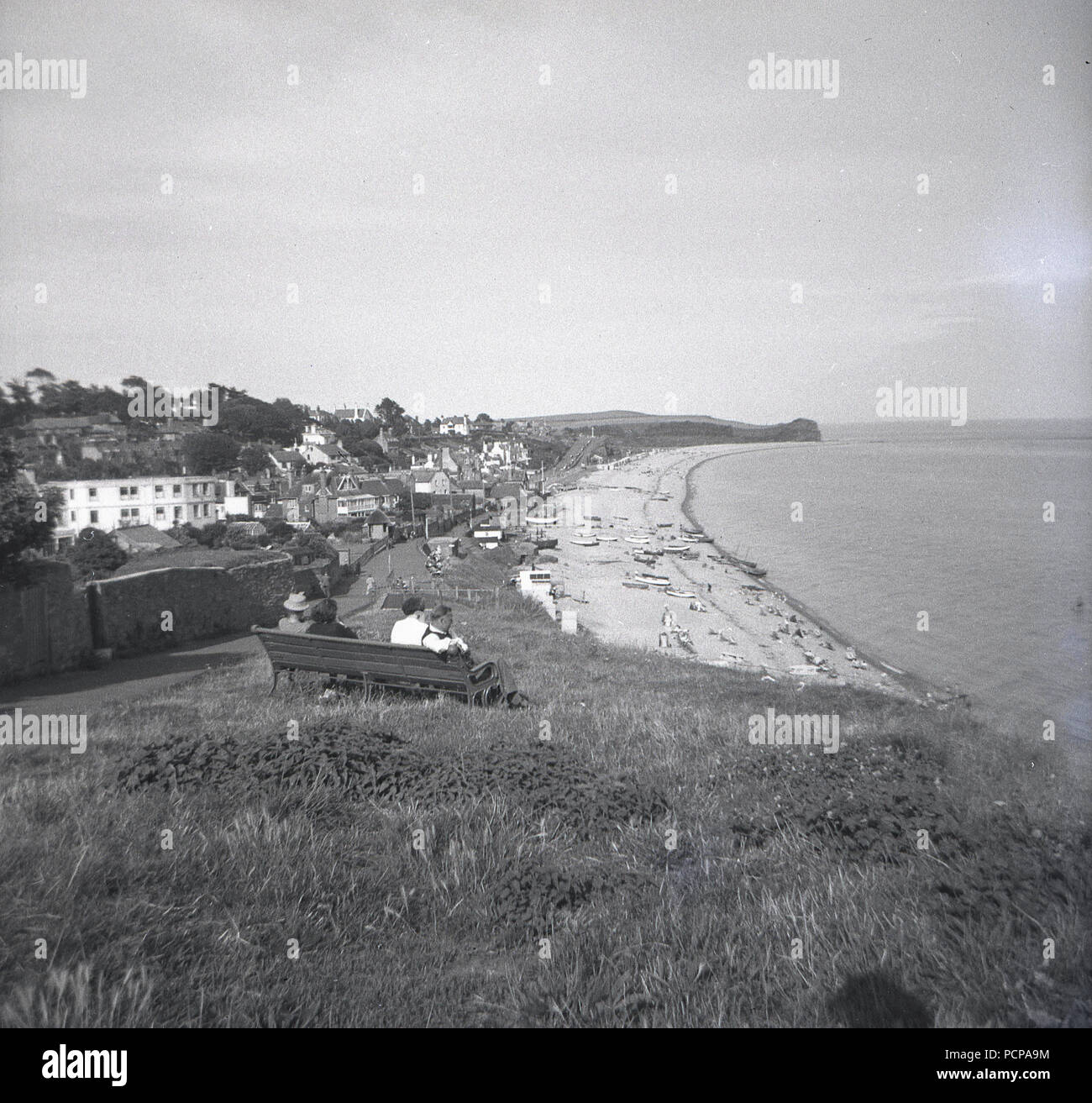 Luglio, 1950, Sidmouth, Devon, la gente seduta su una panchina sul fianco del colle che guarda verso est sulla spiaggia e sul Canale Inglese. Foto Stock