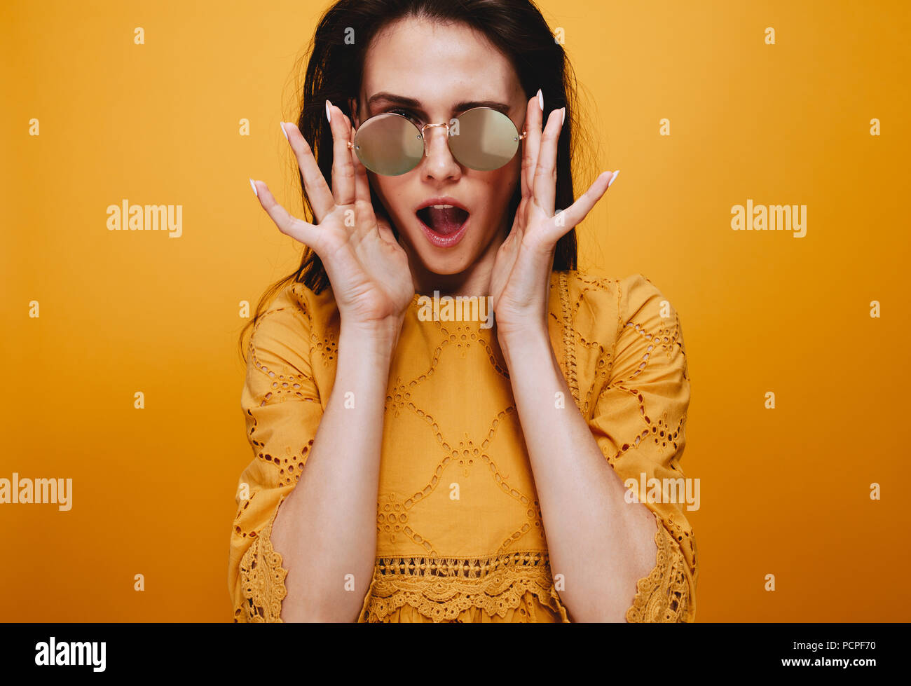 Ritratto del bellissimo modello femminile indossando occhiali da sole funky. Attraente giovane donna in abito arancione guardando la fotocamera con la bocca aperta. Foto Stock