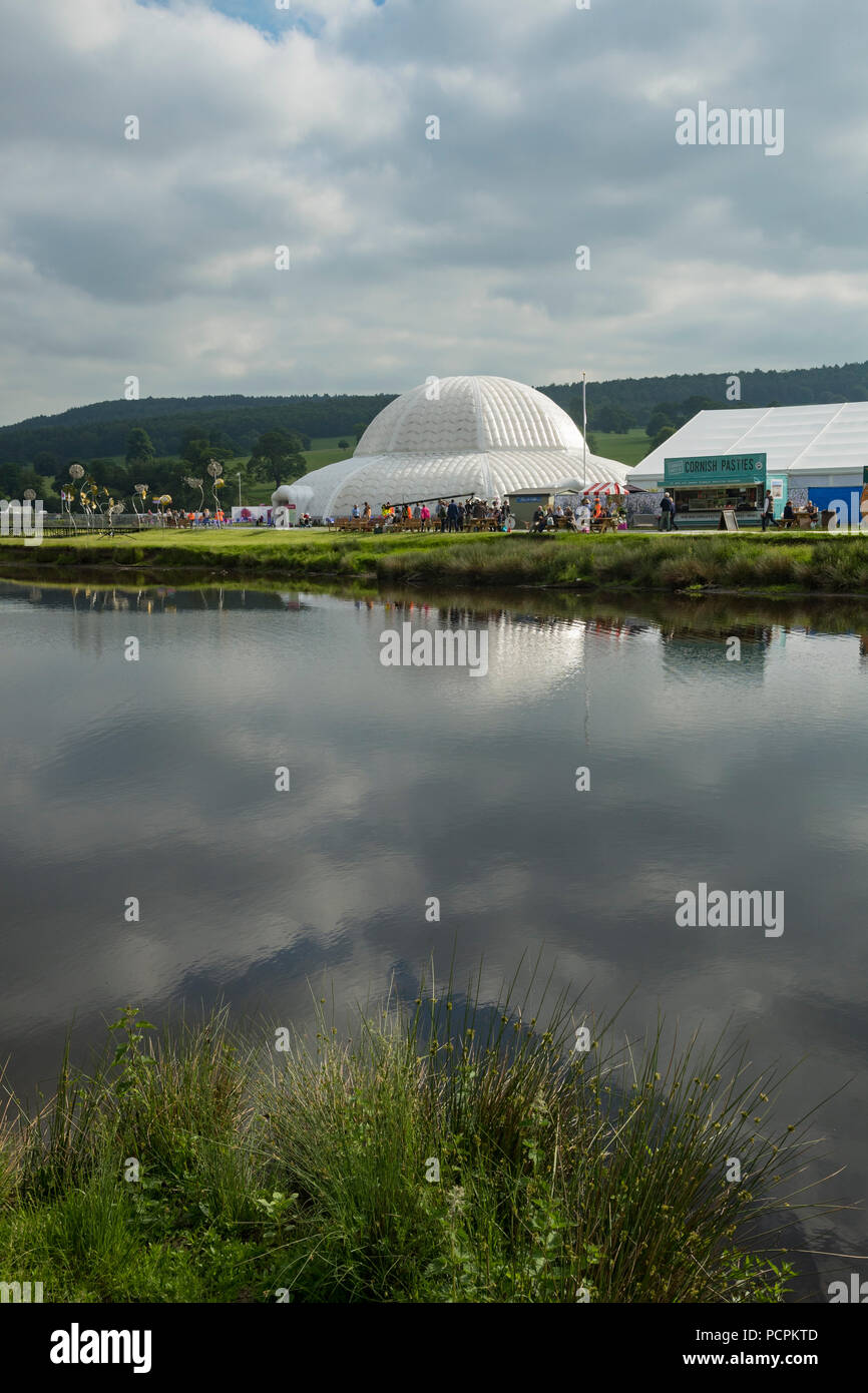 RHS Chatsworth Flower Show showground (persone che visitano, marquee, grande cupola del Conservatorio & cielo nuvoloso si riflette nel fiume) Derbyshire, Inghilterra, Regno Unito. Foto Stock