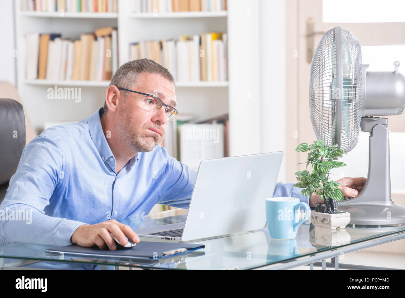 L'uomo soffre dal calore durante il lavoro in ufficio e si tenta di raffreddarsi dalla ventola Foto Stock