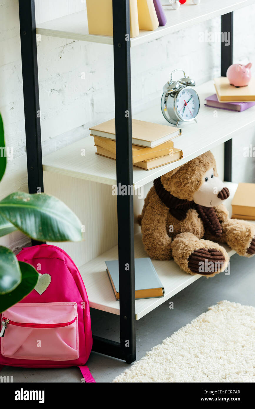 Libri, sveglia e orso di peluche su scaffali e scuola di rosa borsa sul tappeto Foto Stock