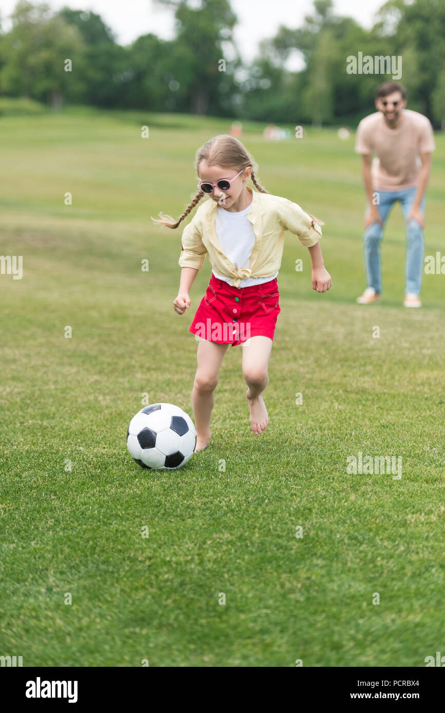 Adorabili bambini in occhiali da sole giocando con il pallone da calcio  mentre il padre in piedi dietro in oark Foto stock - Alamy