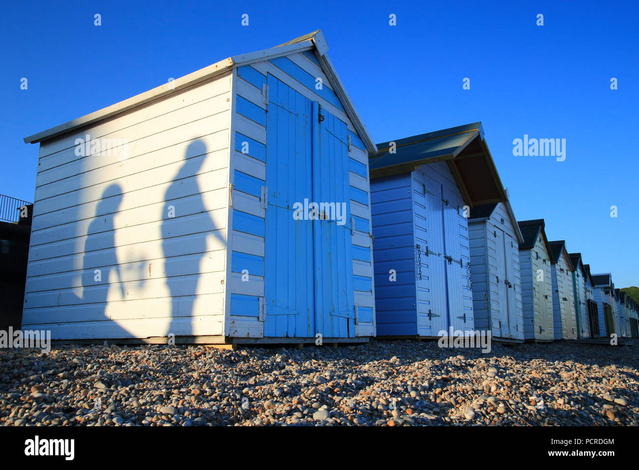 Le ombre delle persone che passano dalla spiaggia bianca di capanne in città costiera di Seaton in East Devon Foto Stock