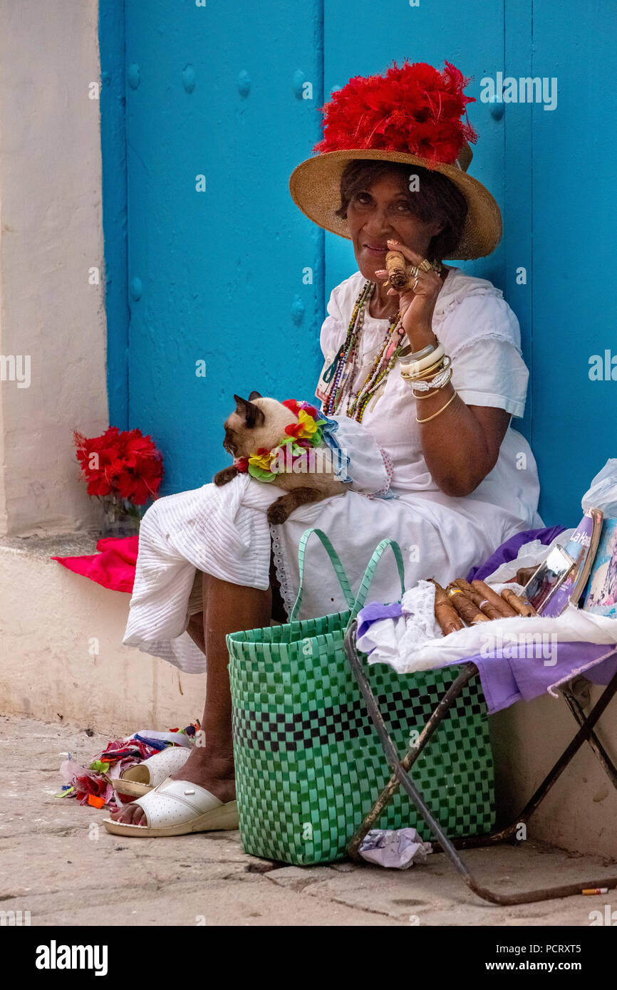 Vecchia donna cubana fuma un sigaro cubano sulla strada e pone con il suo gatto per i turisti, La Habana, Cuba, Caraibi, America centrale, La Habana, Cuba Foto Stock