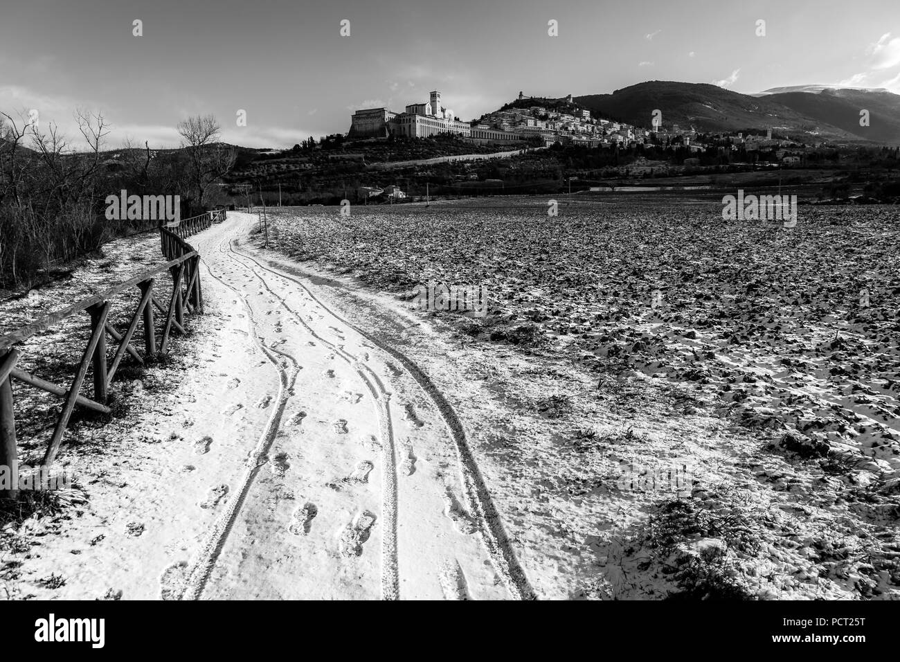 Vista della città di Assisi (Umbria) in inverno, con un campo coperto di neve e cielo con nuvole bianche Foto Stock