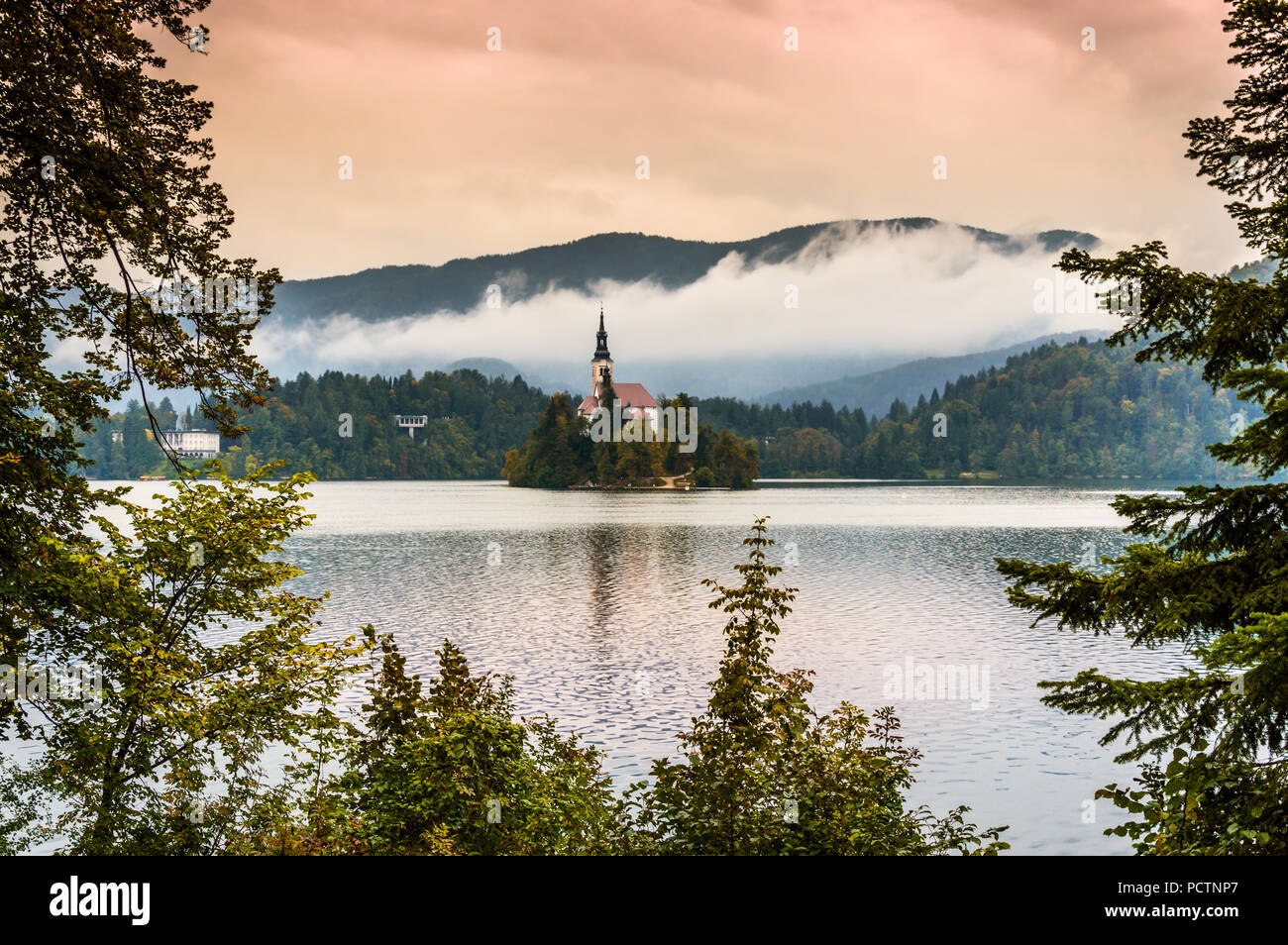 Lago di Bled, Slovenia. Lago di montagna con la piccola isola e chiesa inquadrata con foglie di albero. Stilizzata gli orari di alba e tramonto con colorati sky. Le montagne in Foto Stock