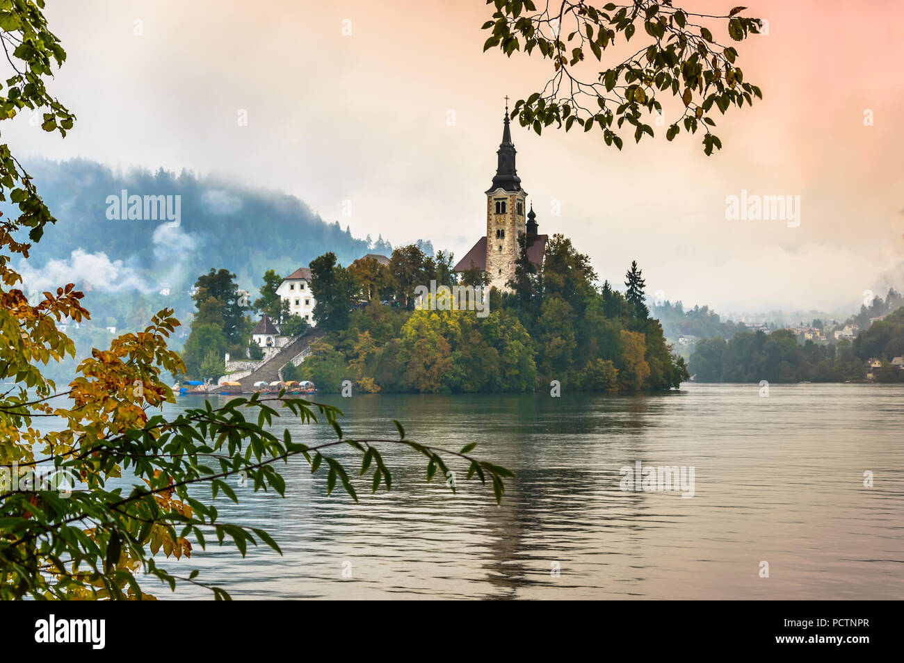 Lago di Bled in autunno, Slovenia. Lago di montagna con la piccola isola e chiesa inquadrata con foglie di albero. Stilizzata gli orari di alba e tramonto con colorati sky. Foto Stock