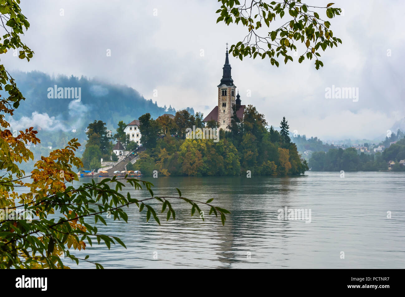 Lago di Bled in autunno, Slovenia. Lago di montagna con la piccola isola e chiesa inquadrata con foglie di albero. Foto Stock