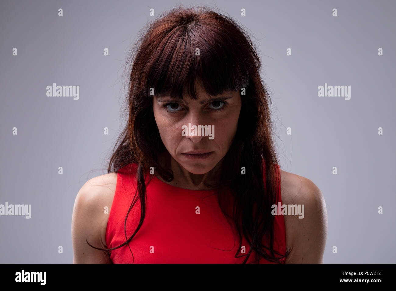 Arrabbiato moody donna fissando attentamente la macchina fotografica con la sua testa abbassata e una solenne manifestazione su un grigio di sfondo per studio Foto Stock