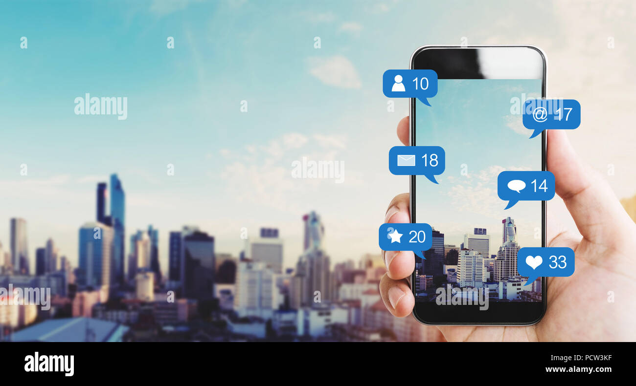 Mano azienda mobile smart phone, con le icone di notifica e sullo sfondo della città Foto Stock
