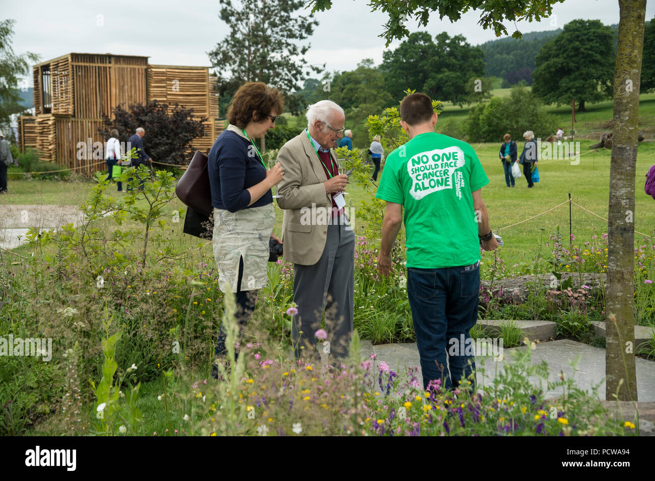 Vista persone caratteristica centrale albero, area lastricata & fiori in bella mostra giardino, - Macmillan Giardino Legacy, RHS Chatsworth Flower Show, Inghilterra, Regno Unito. Foto Stock