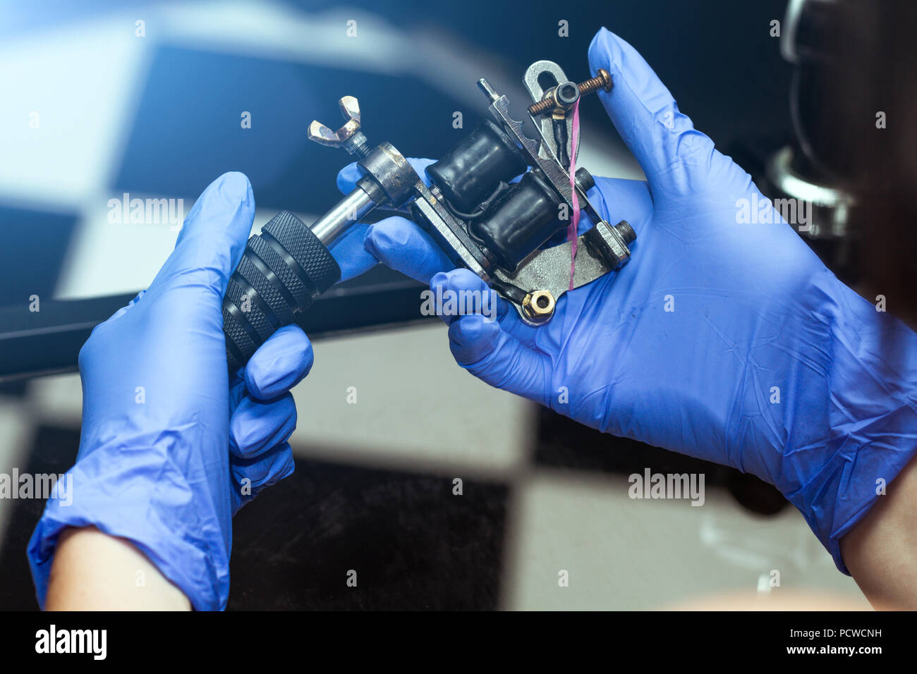 Le mani di un artista del tatuaggio in blu di guanti di gomma di tenere un dermografo. Salone di tatuaggi tema Foto Stock