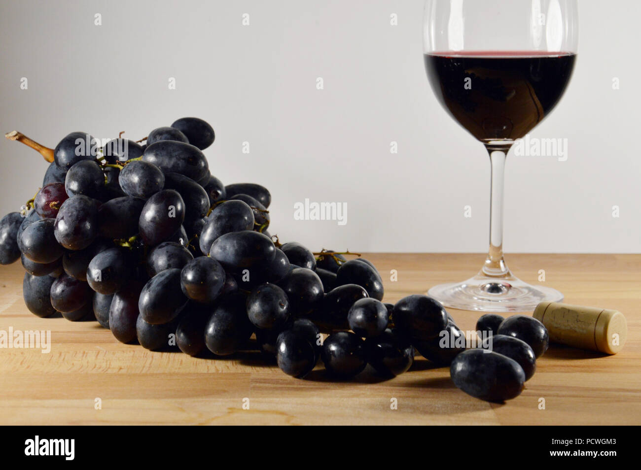 Nero a grappolo di uva con un bicchiere di vino rosso sul pavimento in legno Foto Stock