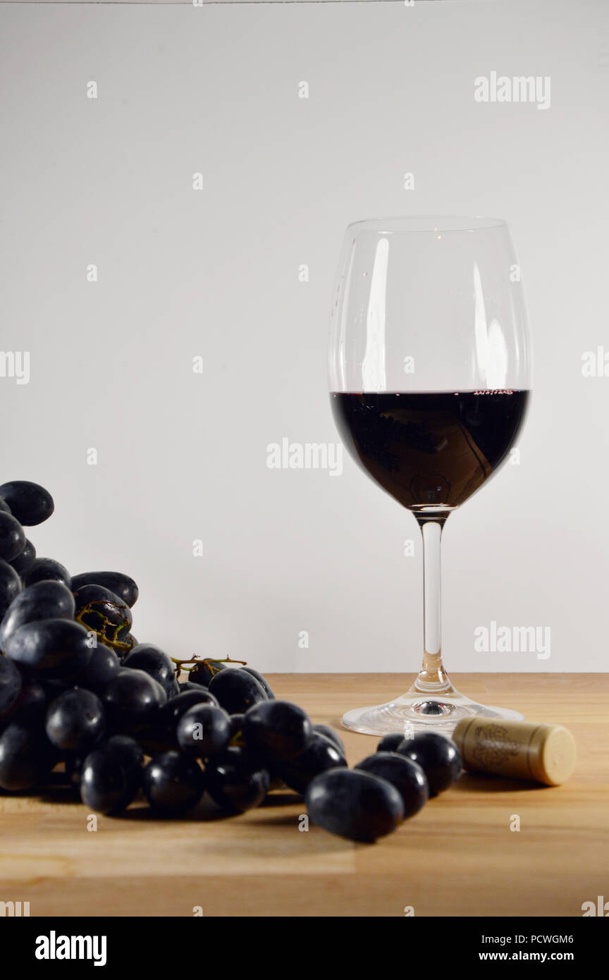 Nero a grappolo di uva con un bicchiere di vino rosso sul pavimento in legno Foto Stock