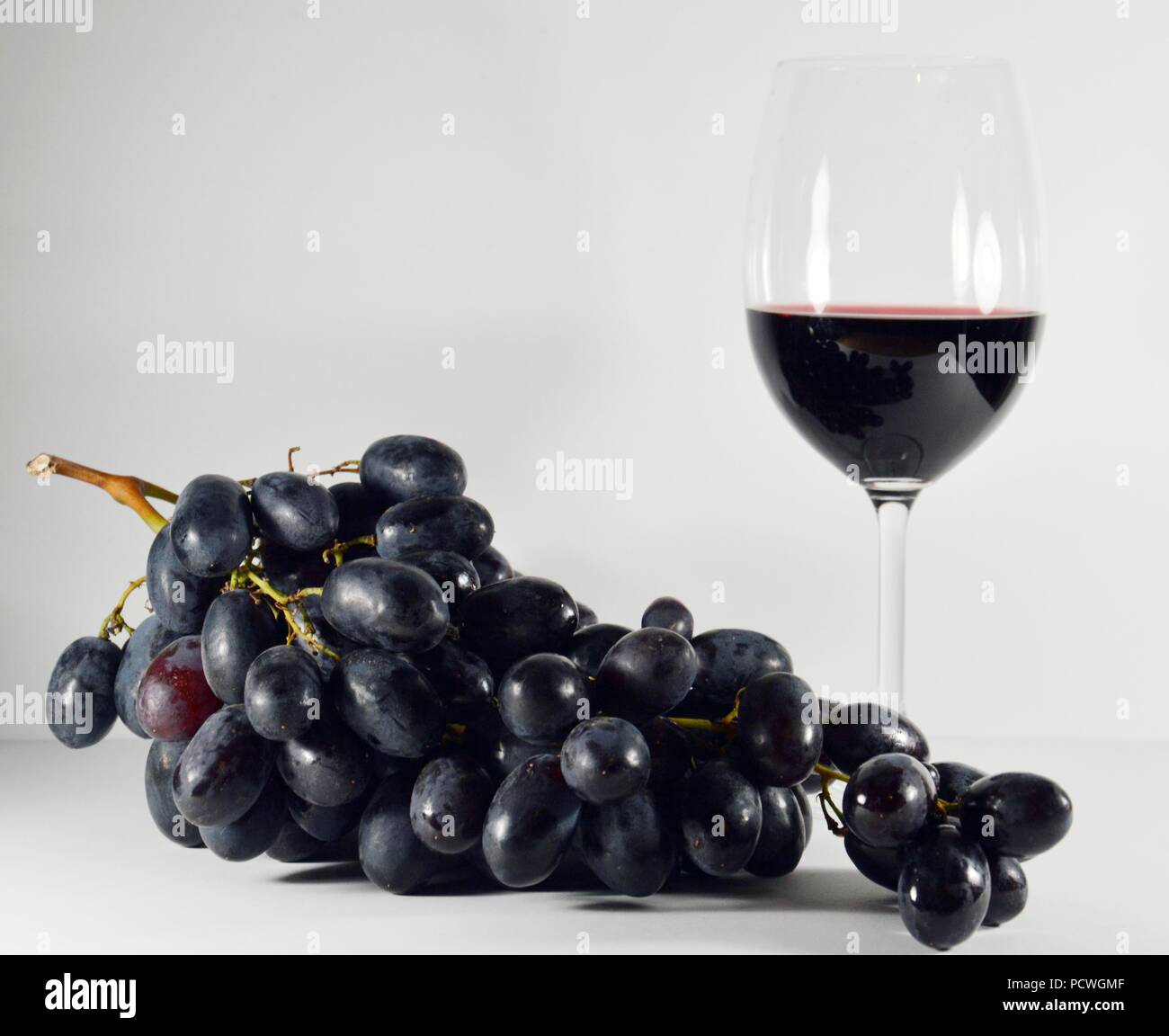 Nero a grappolo di uva con un bicchiere di vino rosso su sfondo bianco Foto Stock