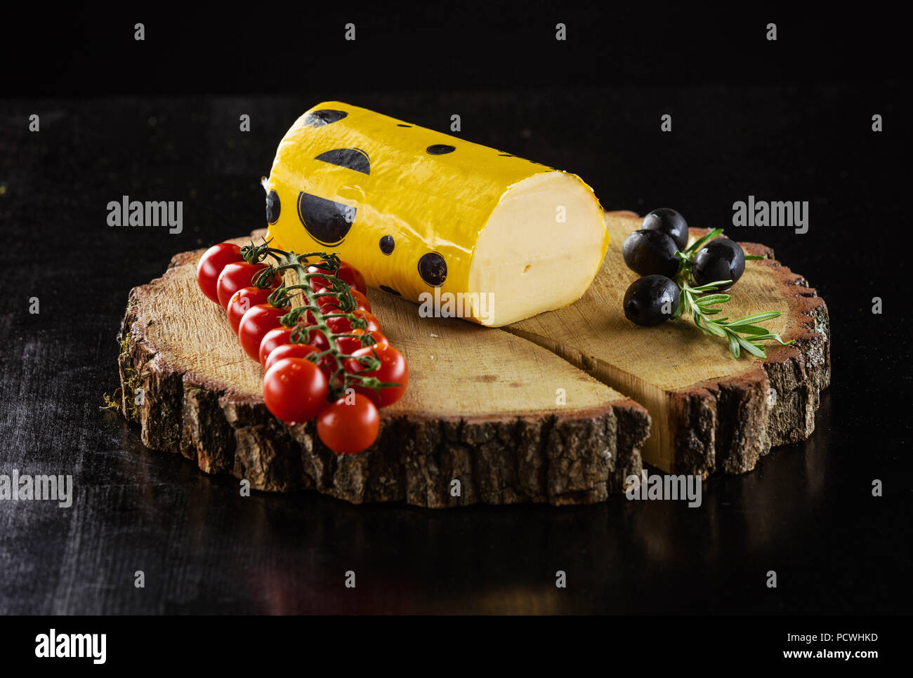 Pezzo di formaggio di salame, pomodorini e olive su tavola di legno sul nero Foto Stock