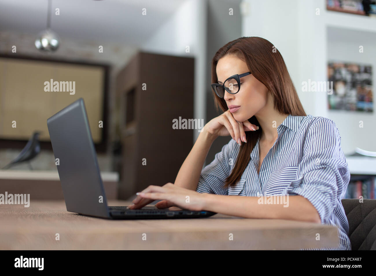 Giovani annoiati donna informale digitando su laptop in interni, la ricerca di lavoro Foto Stock