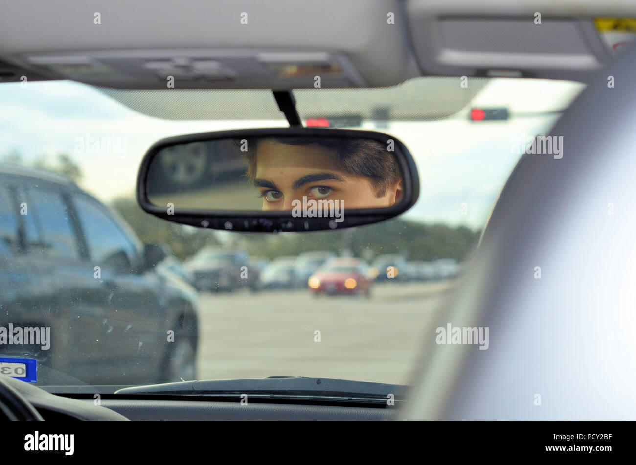 La riflessione del giovane uomo agli occhi esaminando lo specchietto retrovisore di una vettura mentre in corrispondenza di una luce di colore rosso. Foto Stock