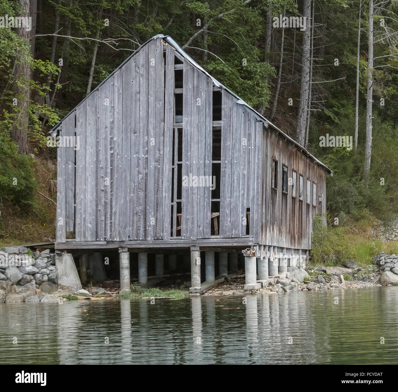 Nella necessità di riparare un vecchio alterò la barca di legno capannone si estende fuori dalla riva, in piedi su un supporto concreto che sarà parzialmente sommerso ad alta marea. Foto Stock