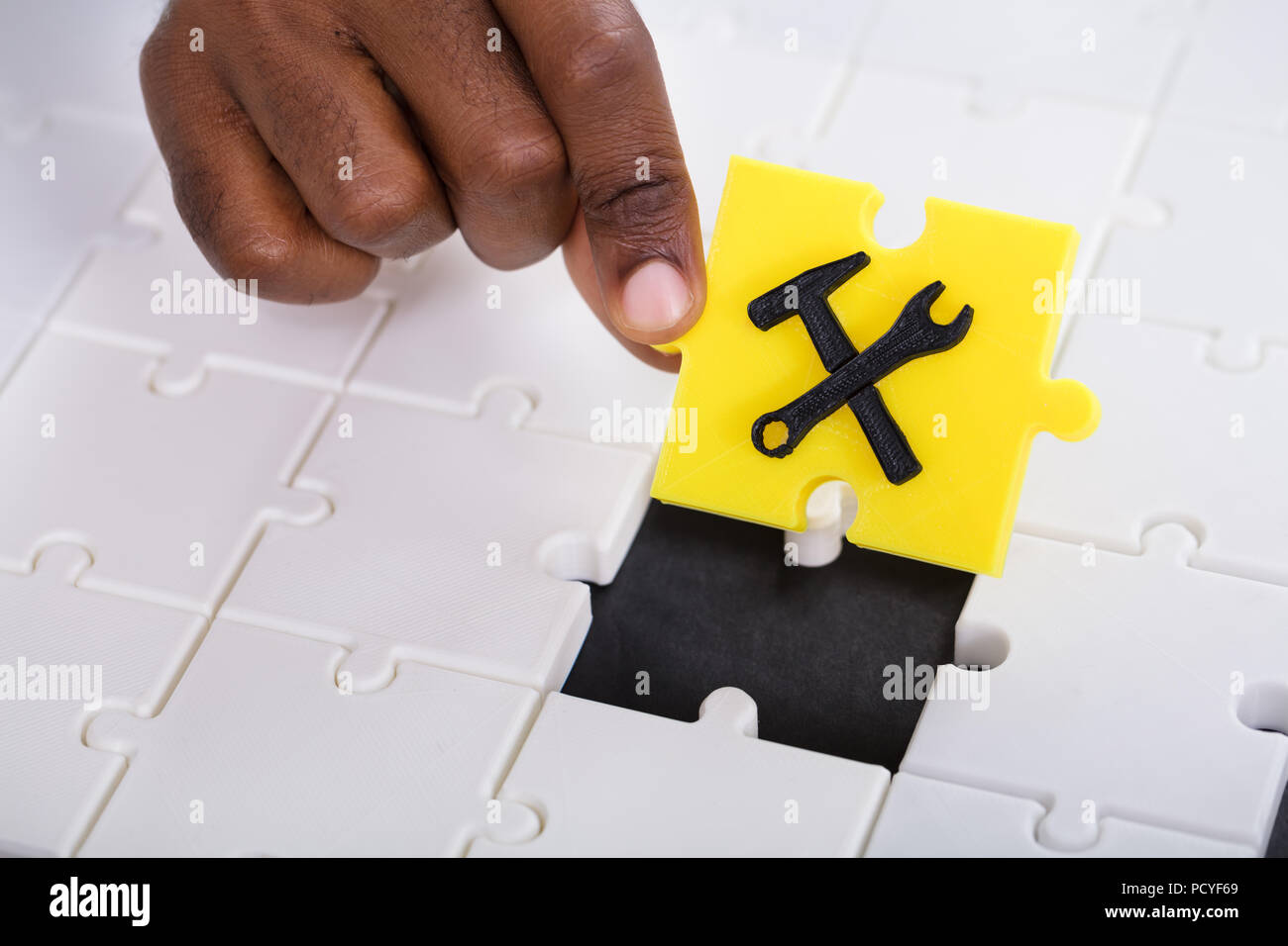 La mano di una persona in possesso di un pezzo di giallo lo strumento di lavoro Puzzle Foto Stock