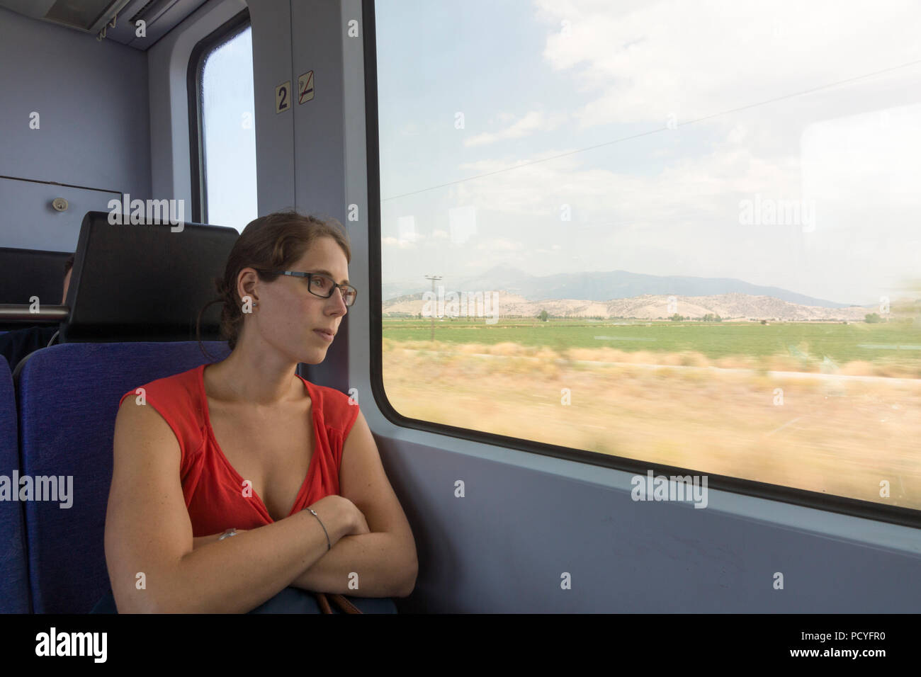 Un turista femminile nel suo ventenne guardando fuori da una finestra del treno a caldo il paesaggio greco impetuoso passato sulla linea Thessaloniki-Larissa Foto Stock