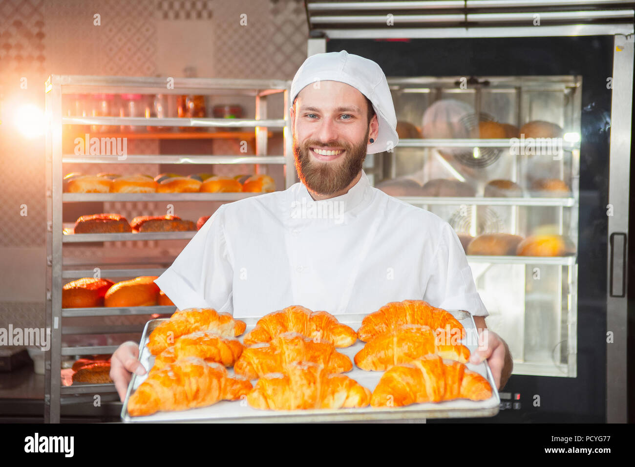 Giovane bello baker holding croissant appena sfornati in mani sullo sfondo del forno. Foto Stock