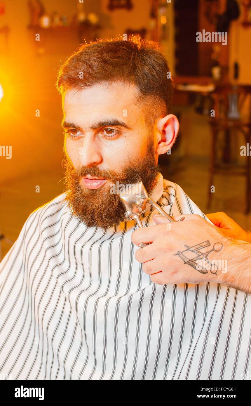 Barbiere tagli una barba di vintage tosatrici per un giovane ragazzo bello  con la barba e baffi. Uomini parrucchiere Foto stock - Alamy