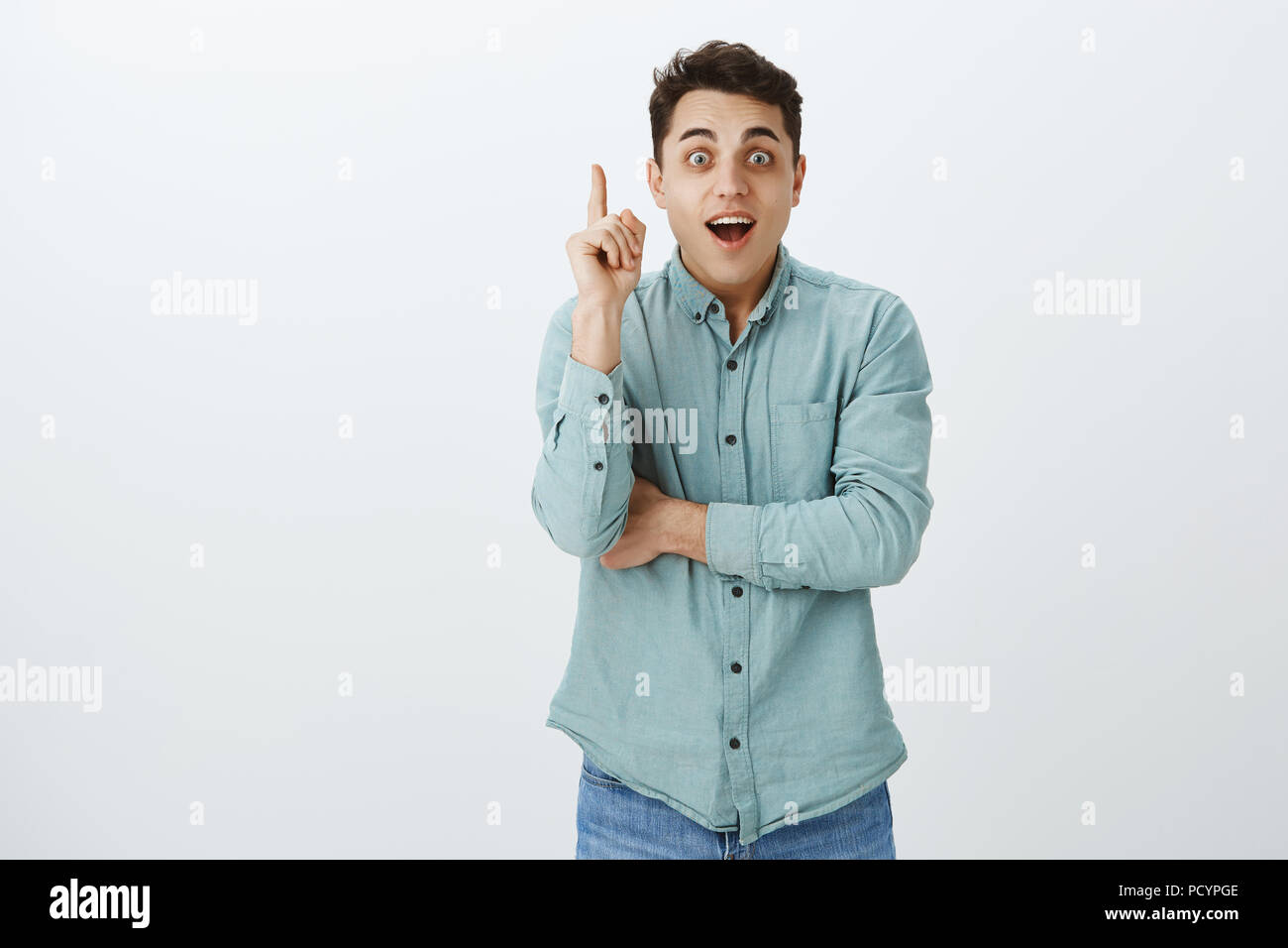 Lieta alleviato bello rasato Uomo in camicia casual, sollevando il dito indice in gesto di Eureka, sorridente ampiamente e con lo sguardo eccitato alla fotocamera, con id Foto Stock